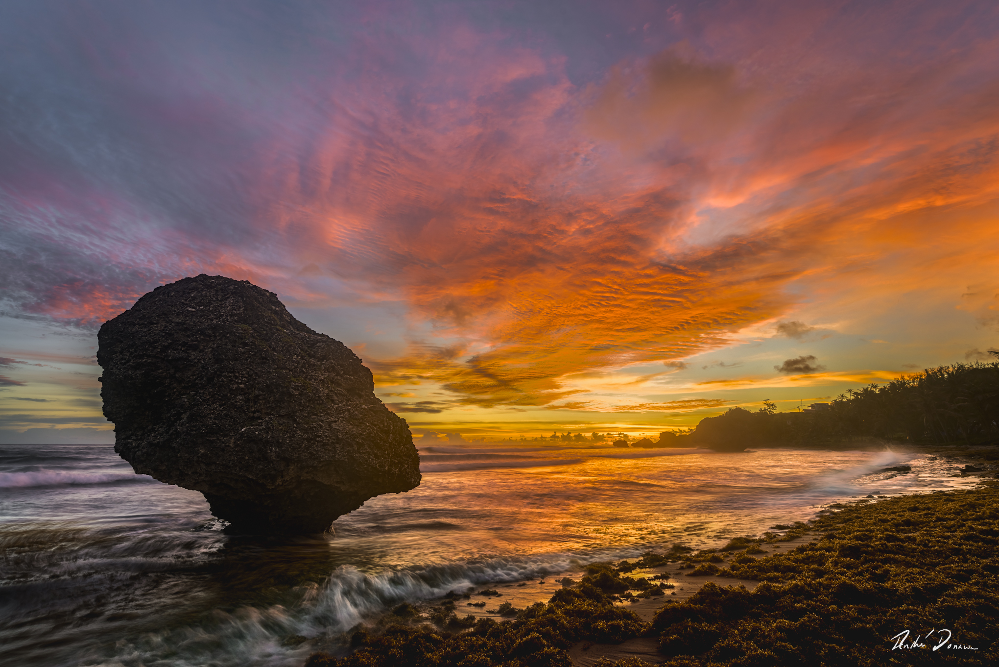 A large rock in the sea, a colourful sunrise and breaking waves at Bathsheba, Barbados