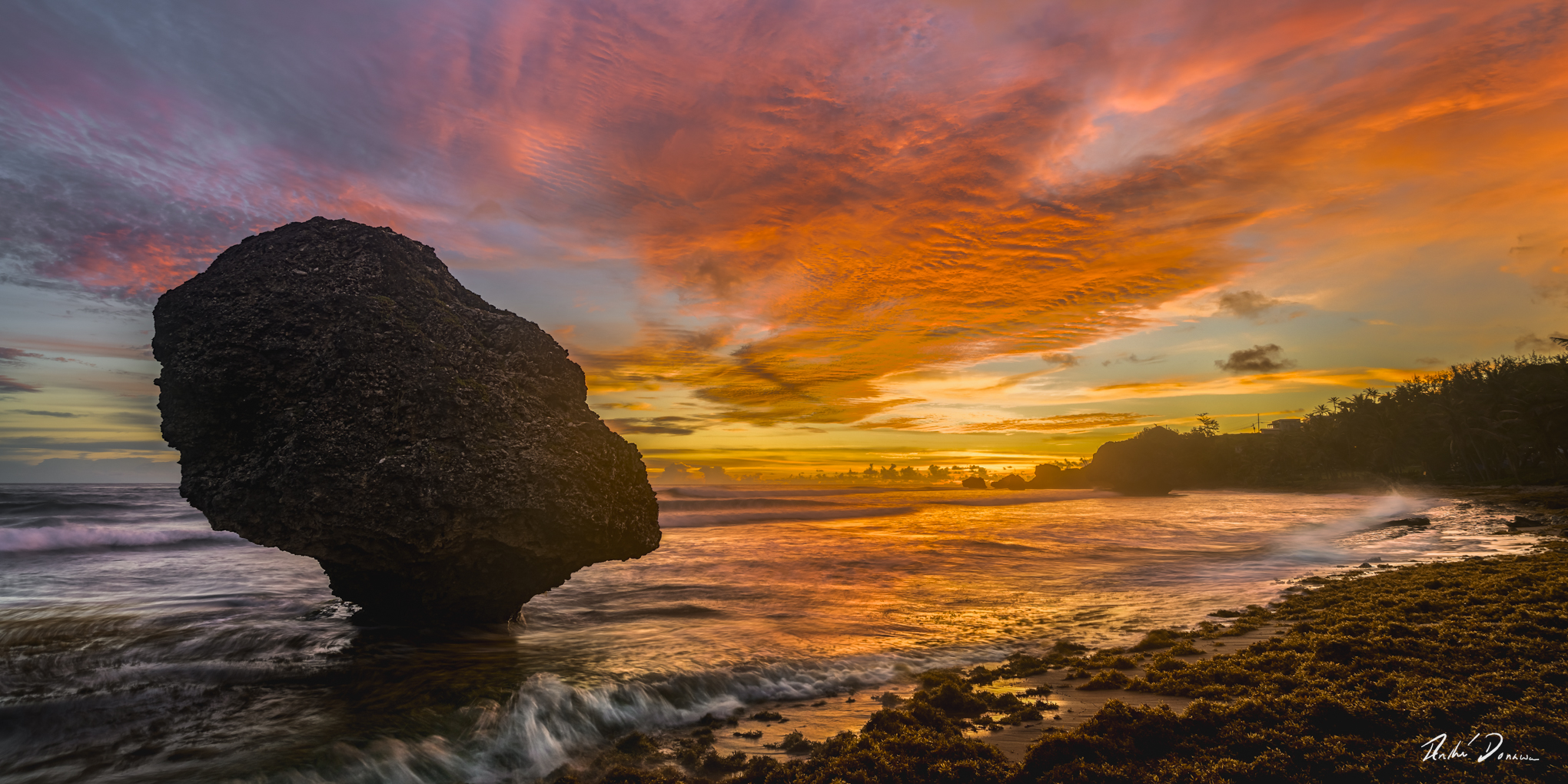 A large rock in the sea, a colourful sunrise and breaking waves at Bathsheba, Barbados